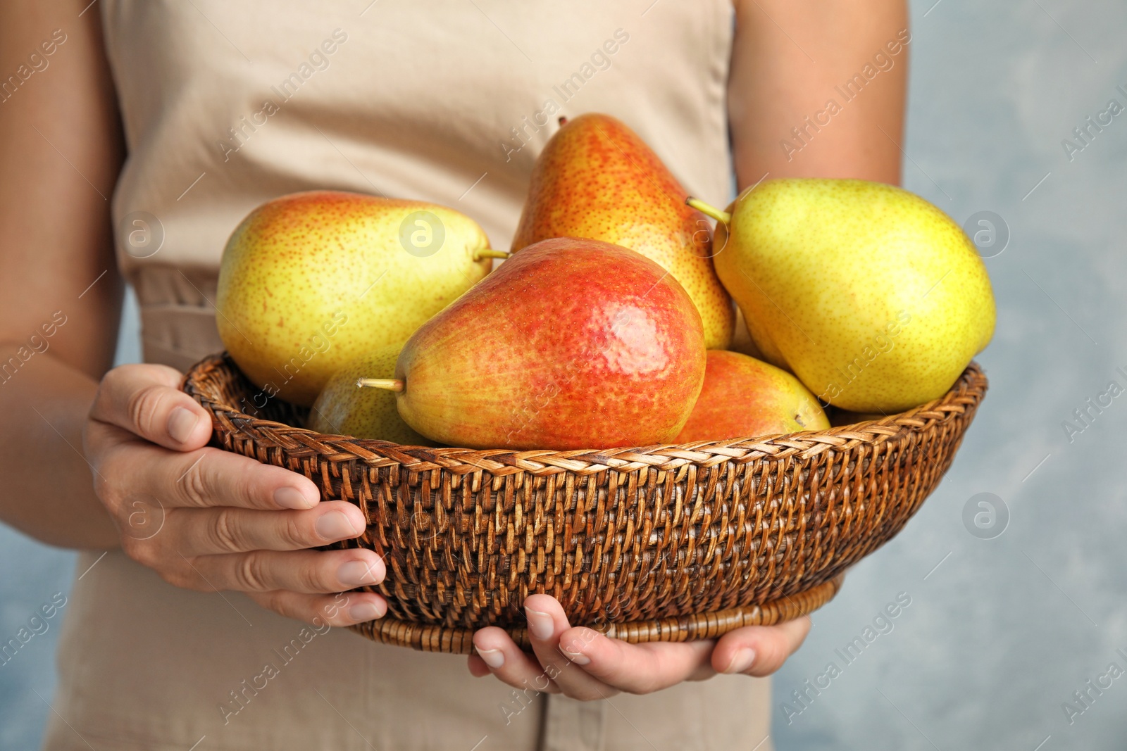 Photo of Woman holding wicker basket with ripe juicy pears on blue background, closeup