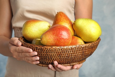 Woman holding wicker basket with ripe juicy pears on blue background, closeup