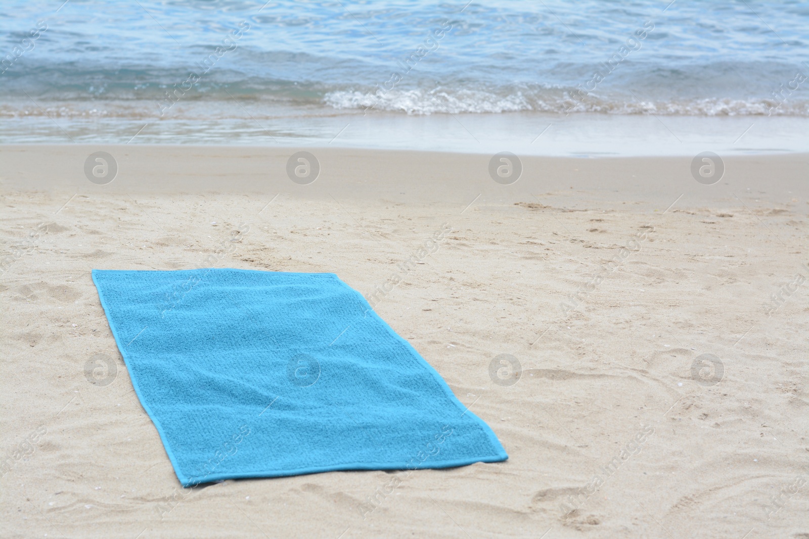 Photo of Blue towel on sandy beach near sea, space for text