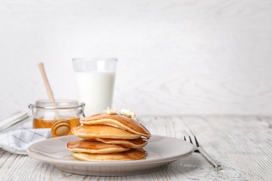 Tasty pancakes with honey and butter on table