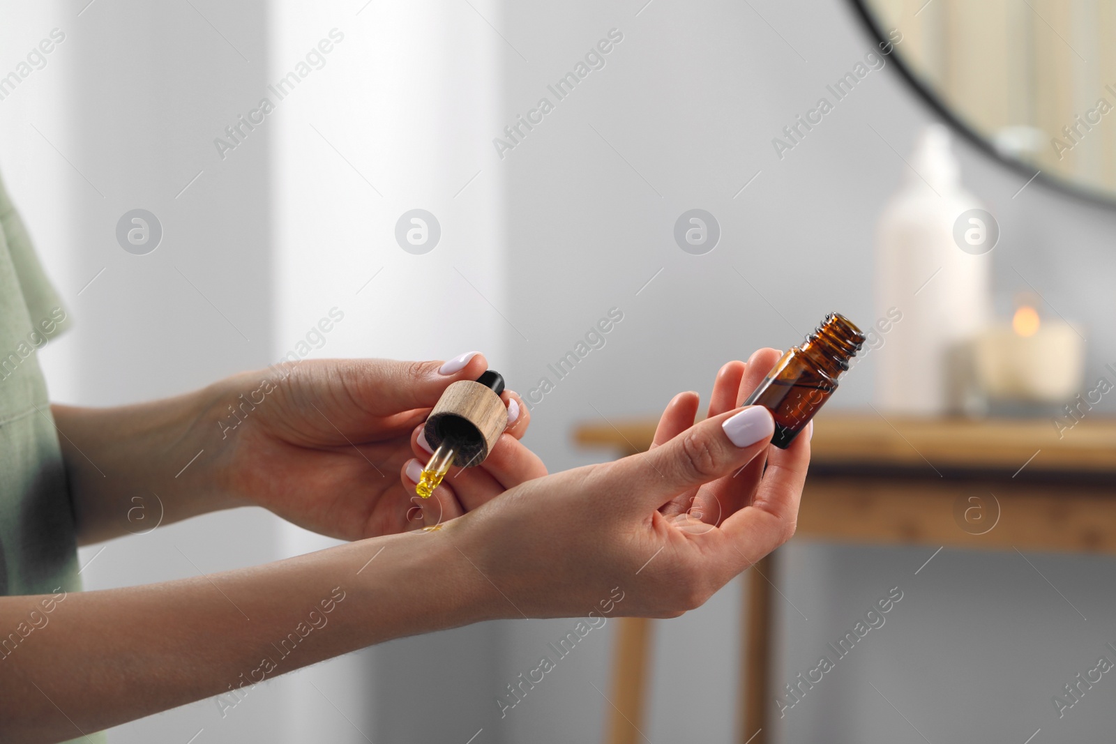 Photo of Young woman applying essential oil on wrist indoors, closeup