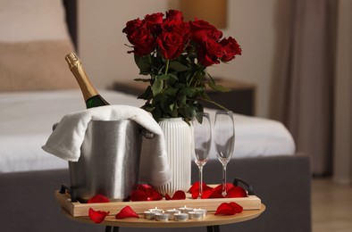 Photo of Honeymoon. Sparkling wine, glasses and bouquet of roses on wooden table in room