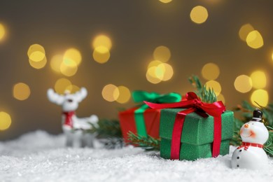 Photo of Gift boxes and Christmas decor on artificial snow against blurred festive lights, space for text