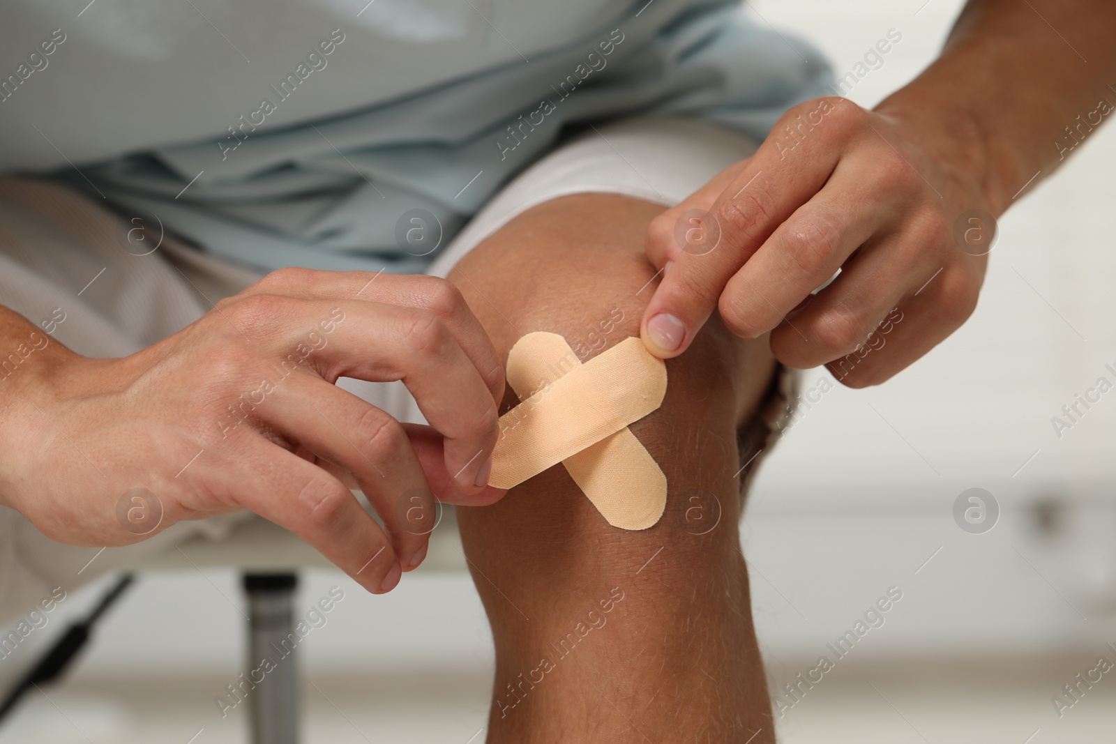 Photo of Man putting sticking plasters onto knee indoors, closeup
