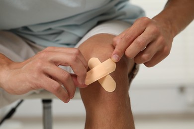 Man putting sticking plasters onto knee indoors, closeup