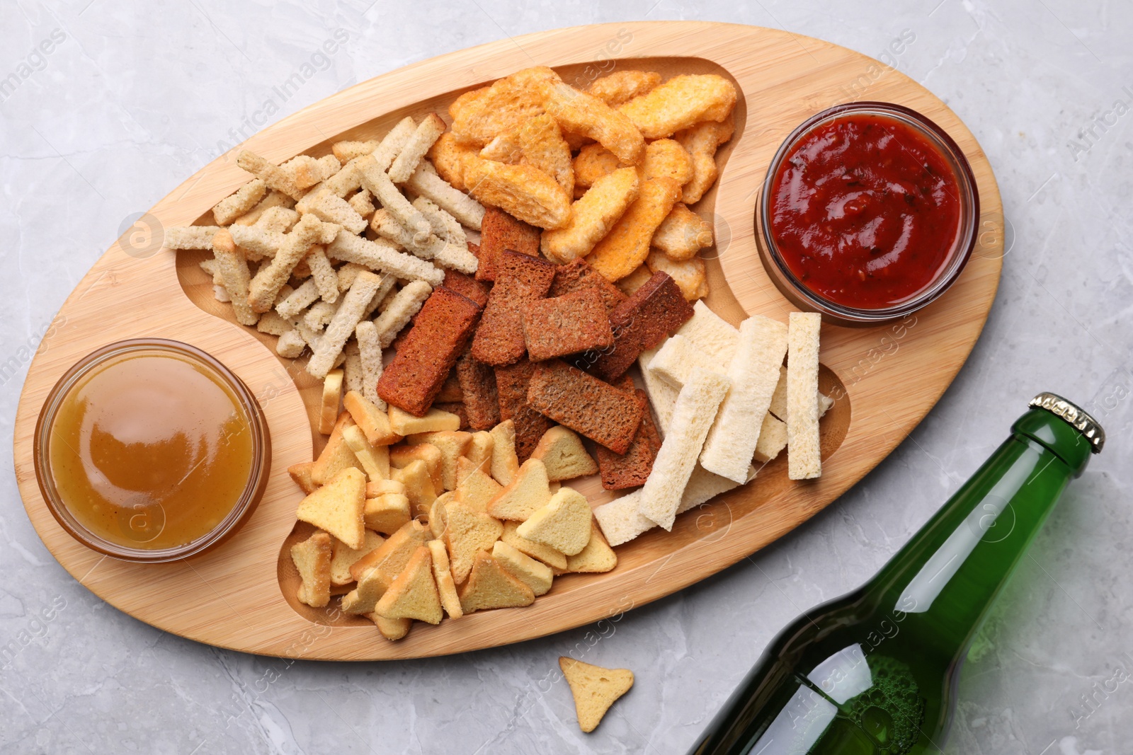 Photo of Different crispy rusks served with dip sauces and beer on light marble table, flat lay