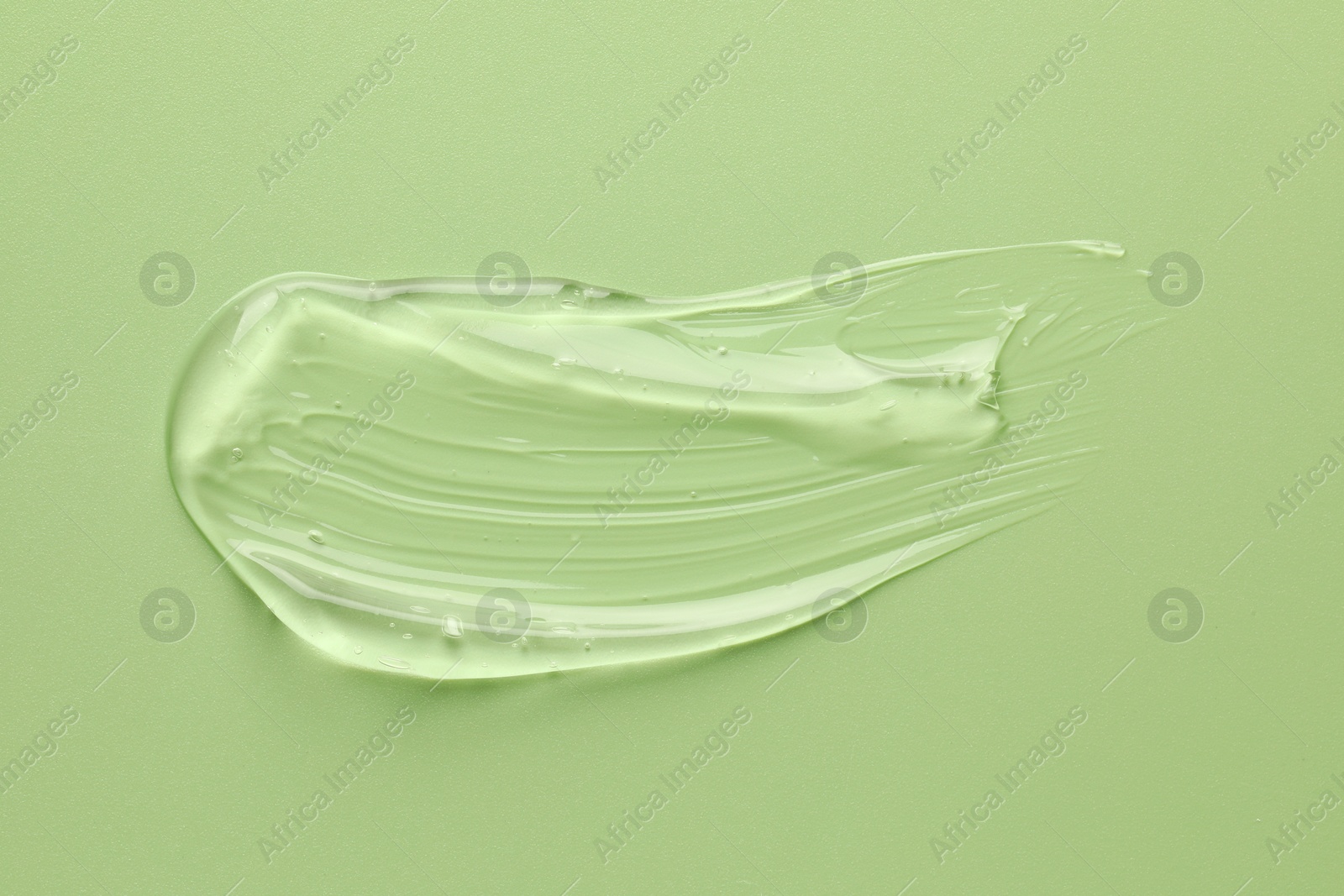 Photo of Smear of clear cosmetic gel on light green background, top view