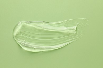 Smear of clear cosmetic gel on light green background, top view