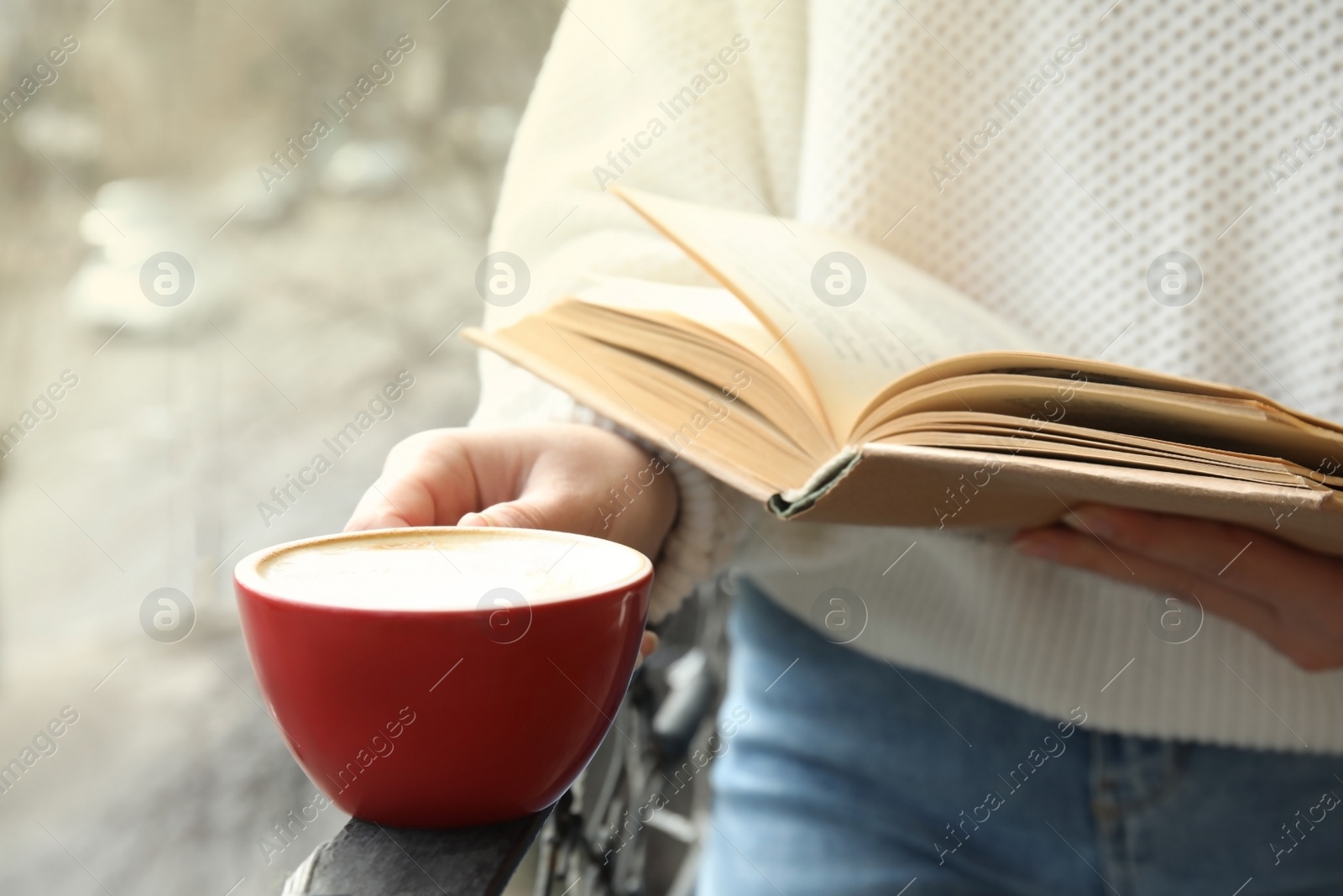 Photo of Woman with cup of coffee reading book outdoors, closeup