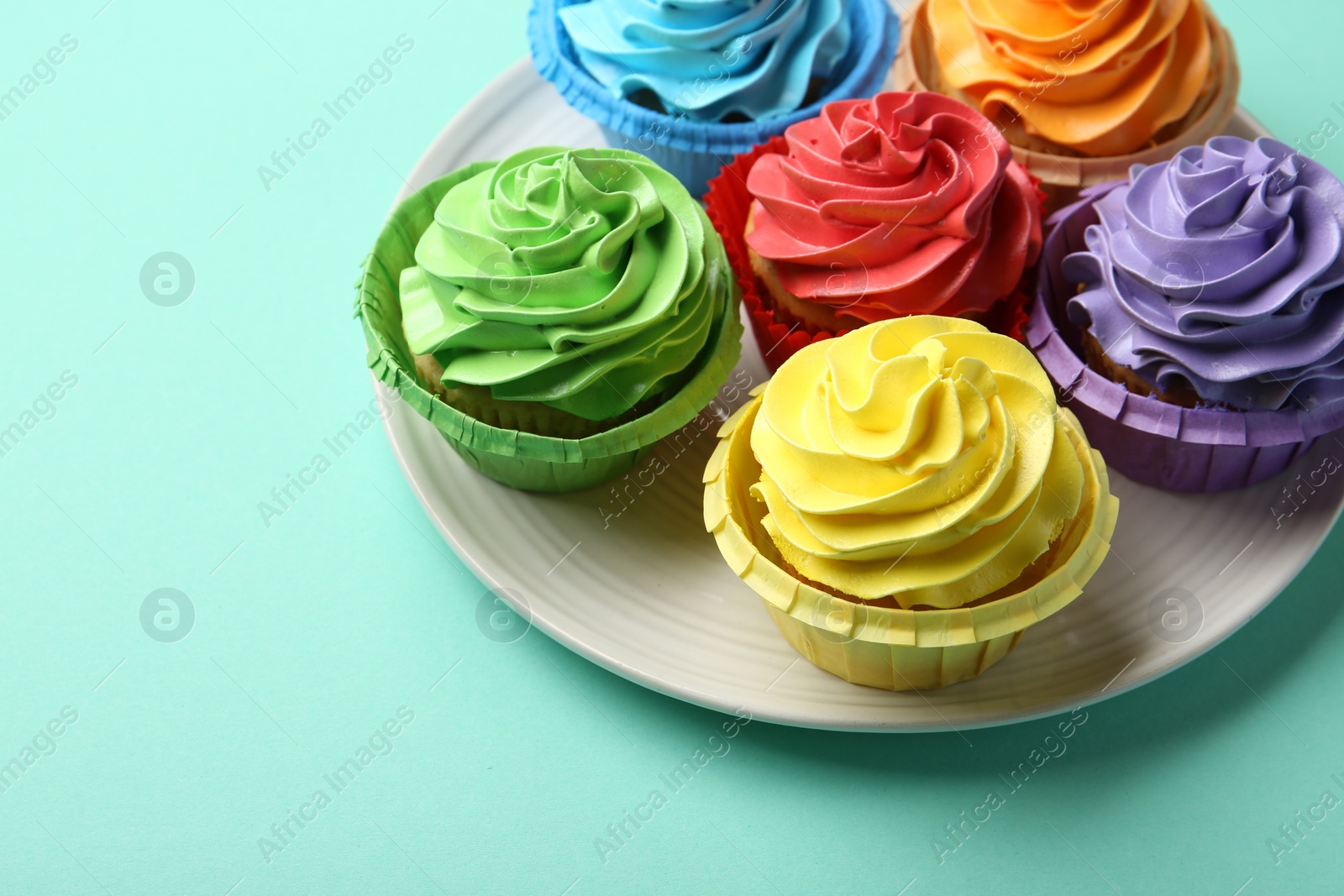 Photo of Plate with delicious bright cupcakes on turquoise background. Space for text