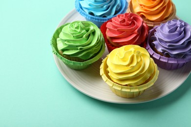 Photo of Plate with delicious bright cupcakes on turquoise background. Space for text