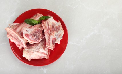 Photo of Plate with raw chopped meaty bones and basil on grey table, top view. Space for text