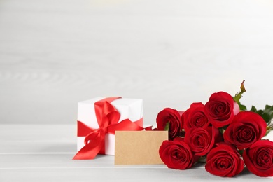 Beautiful red roses, blank card and gift box on white table, space for text. St. Valentine's day celebration