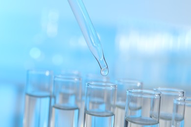 Photo of Dripping liquid from pipette into test tube on light background, closeup