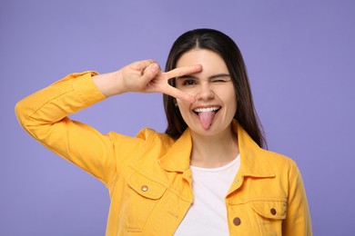 Photo of Happy young woman showing her tongue on purple background