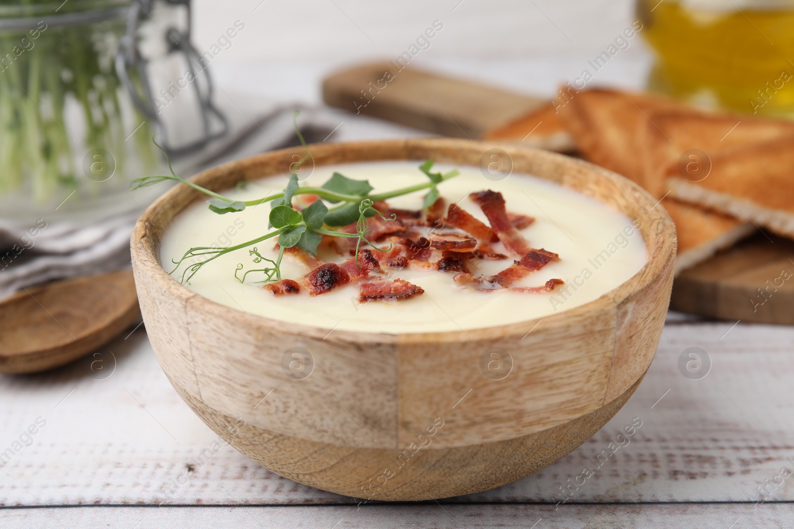 Photo of Delicious potato soup with bacon and microgreens in bowl on wooden table, closeup