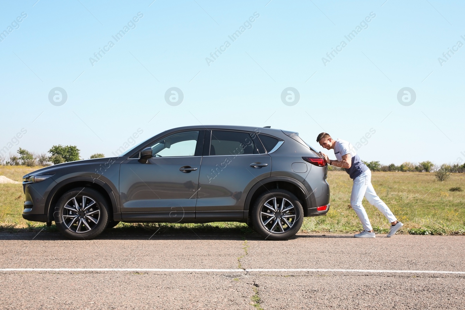 Photo of Man pushing broken car along country road