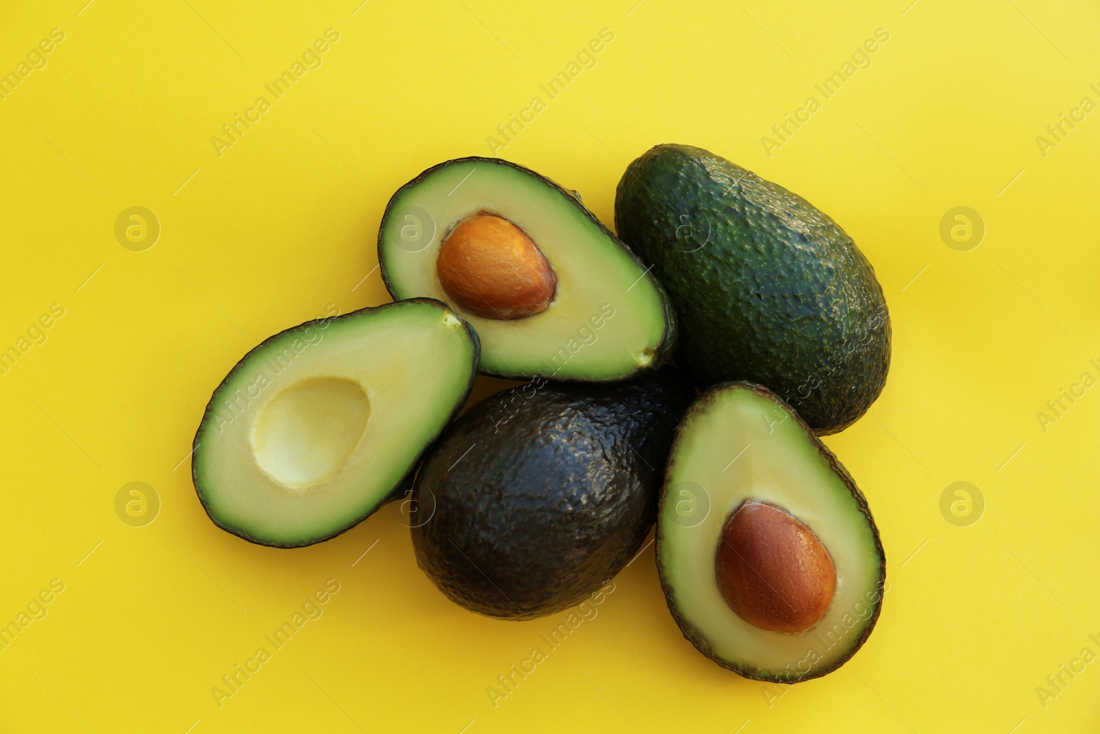 Photo of Fresh whole and cut avocados on yellow background, flat lay