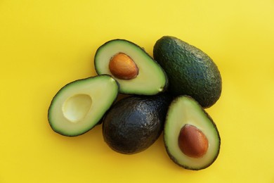 Fresh whole and cut avocados on yellow background, flat lay