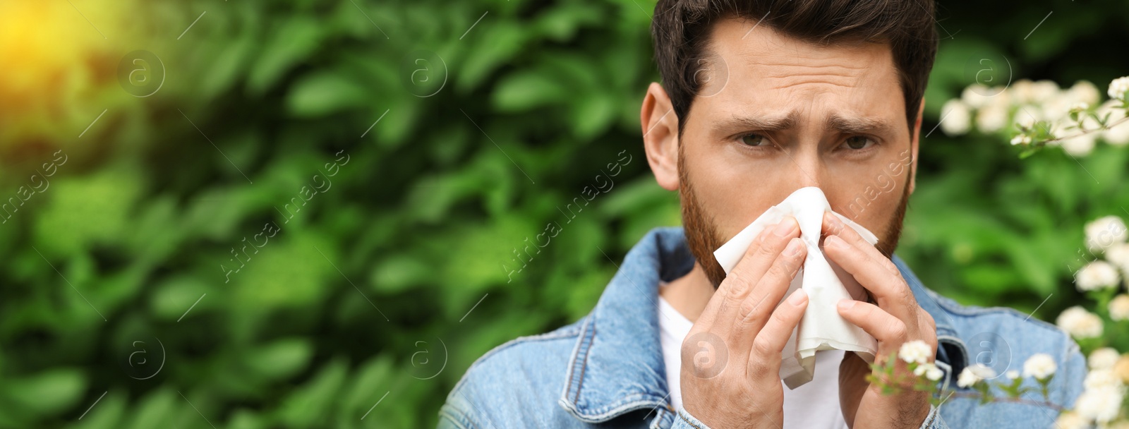 Image of Man suffering from seasonal pollen allergy near blossoming tree on spring day. Banner design with space for text