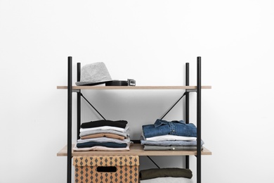 Photo of Shelves unit with stacked clothes and box near white wall