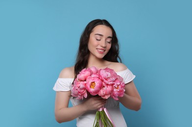 Photo of Beautiful young woman with bouquet of pink peonies on light blue background
