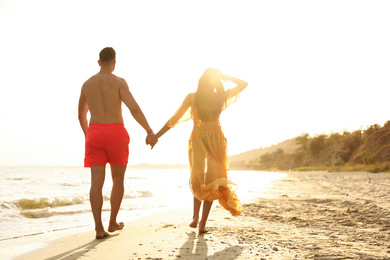 Photo of Lovely couple walking together on beach at sunset, back view