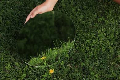 Girl holding round mirror reflecting green grass and dandelion, closeup