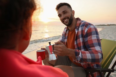 Couple enjoying hot drink on seashore. Beach camping