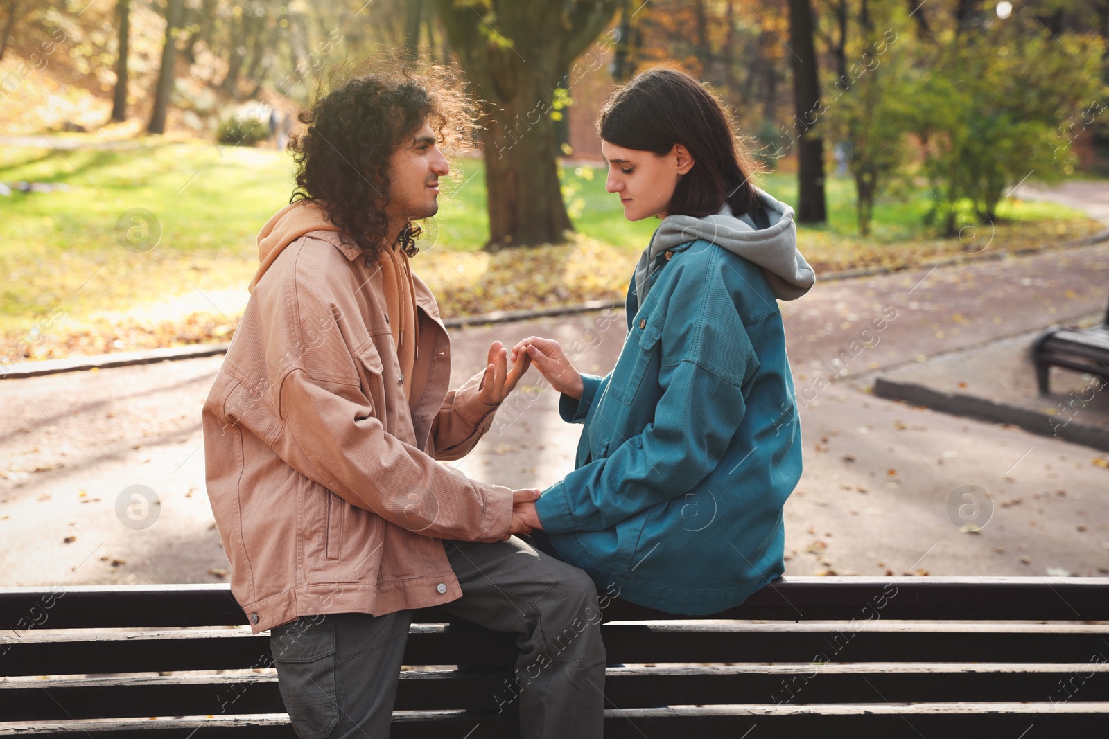 Photo of Young couple spending time together on wooden bench in autumn park, space for text. Dating agency