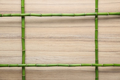 Photo of Frame made of green bamboo stems on wooden background. Space for text