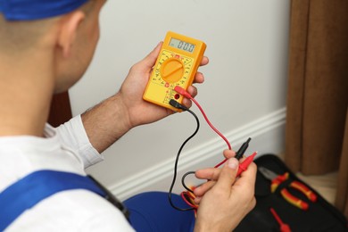 Photo of Professional electrician with voltage tester indoors, closeup