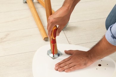 Photo of Man with screwdriver assembling furniture on floor, closeup