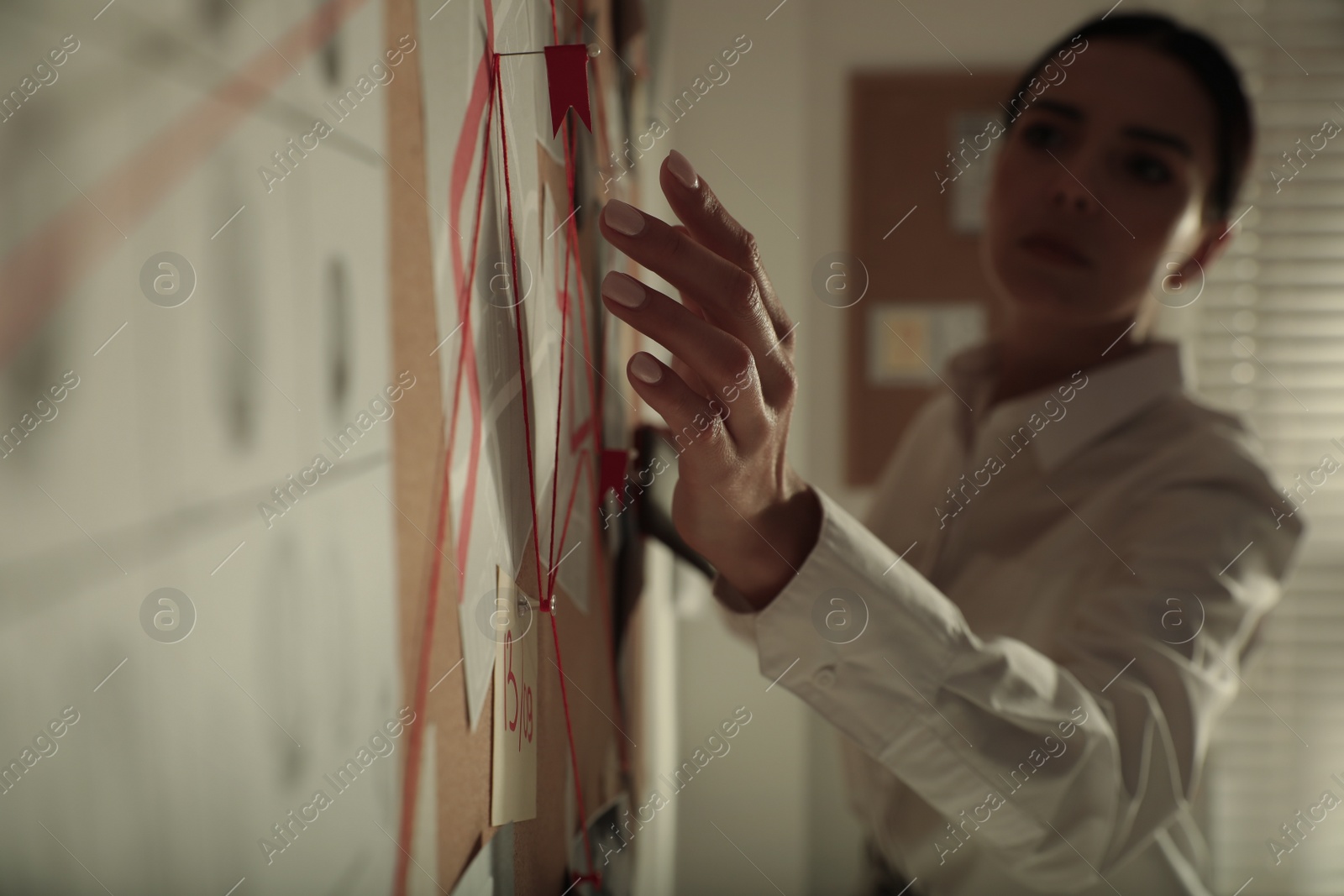 Photo of Detective looking at evidence board in office, focus on hand