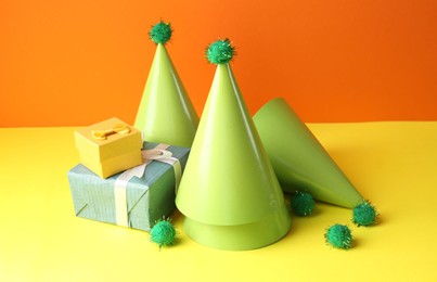 Party hats and gift boxes on yellow table against orange background