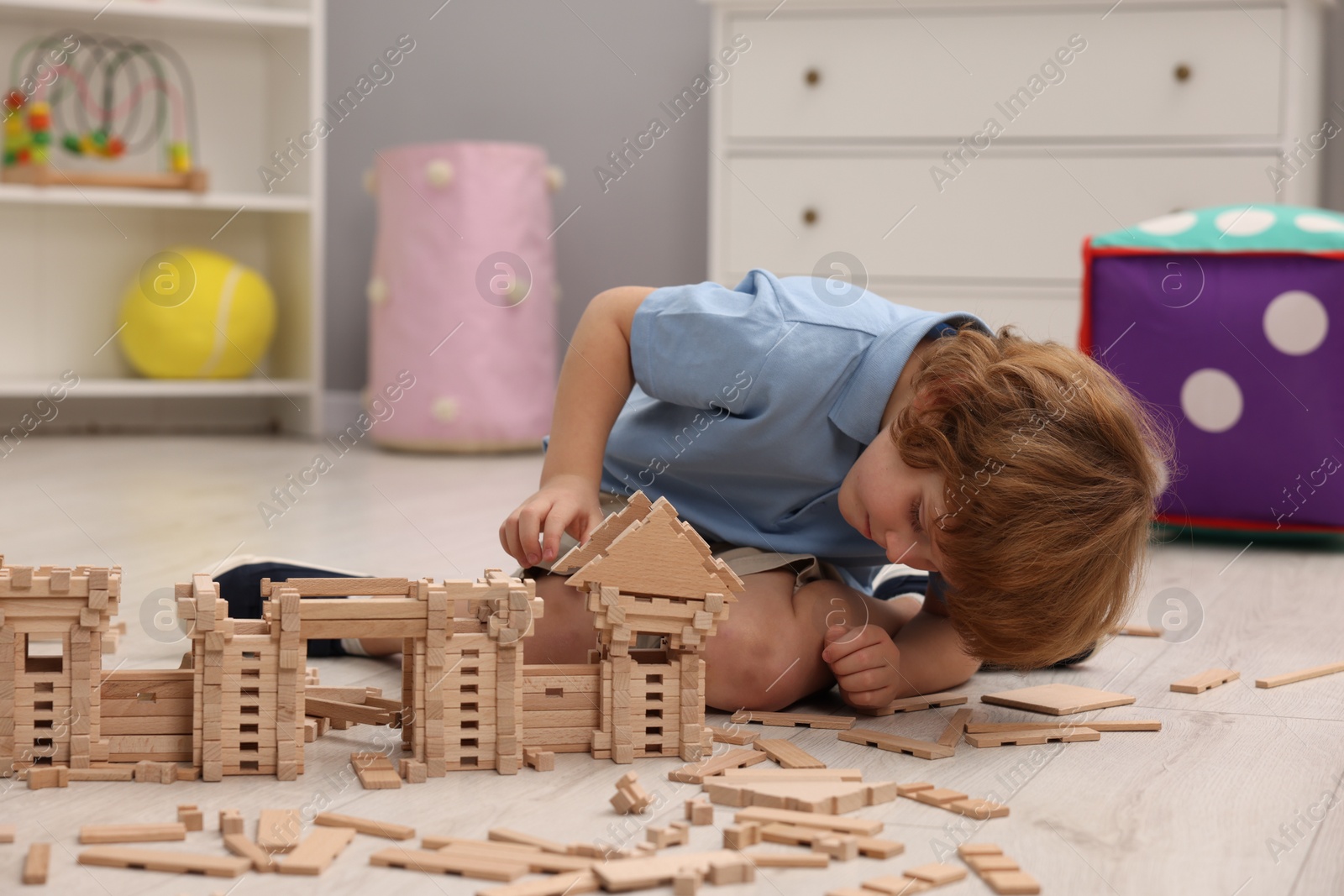 Photo of Little boy playing with wooden construction set on floor in room. Child's toy