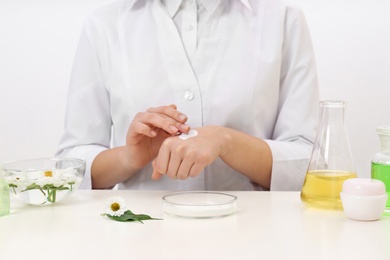Female dermatologist testing skin care product at table, closeup