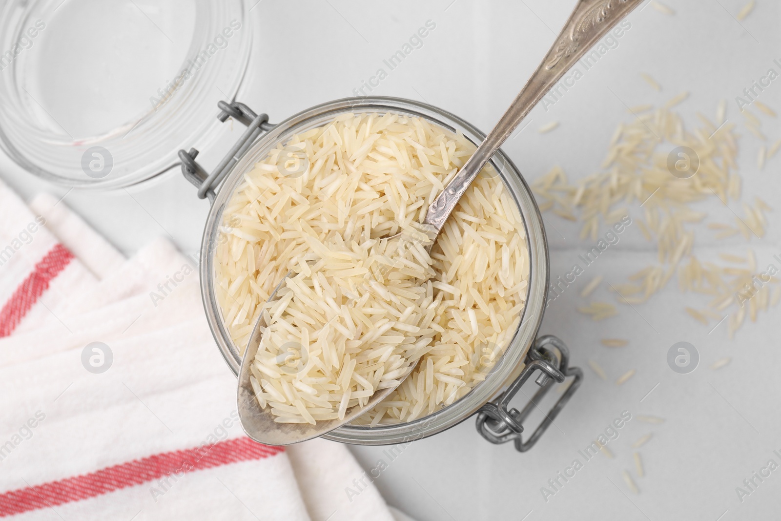 Photo of Glass jar and spoon with raw rice on white tiled table, top view