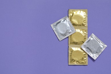 Photo of Condom packages on violet background, flat lay and space for text. Safe sex