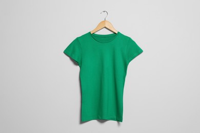 Photo of Hanger with green t-shirt on light wall. Mockup for design
