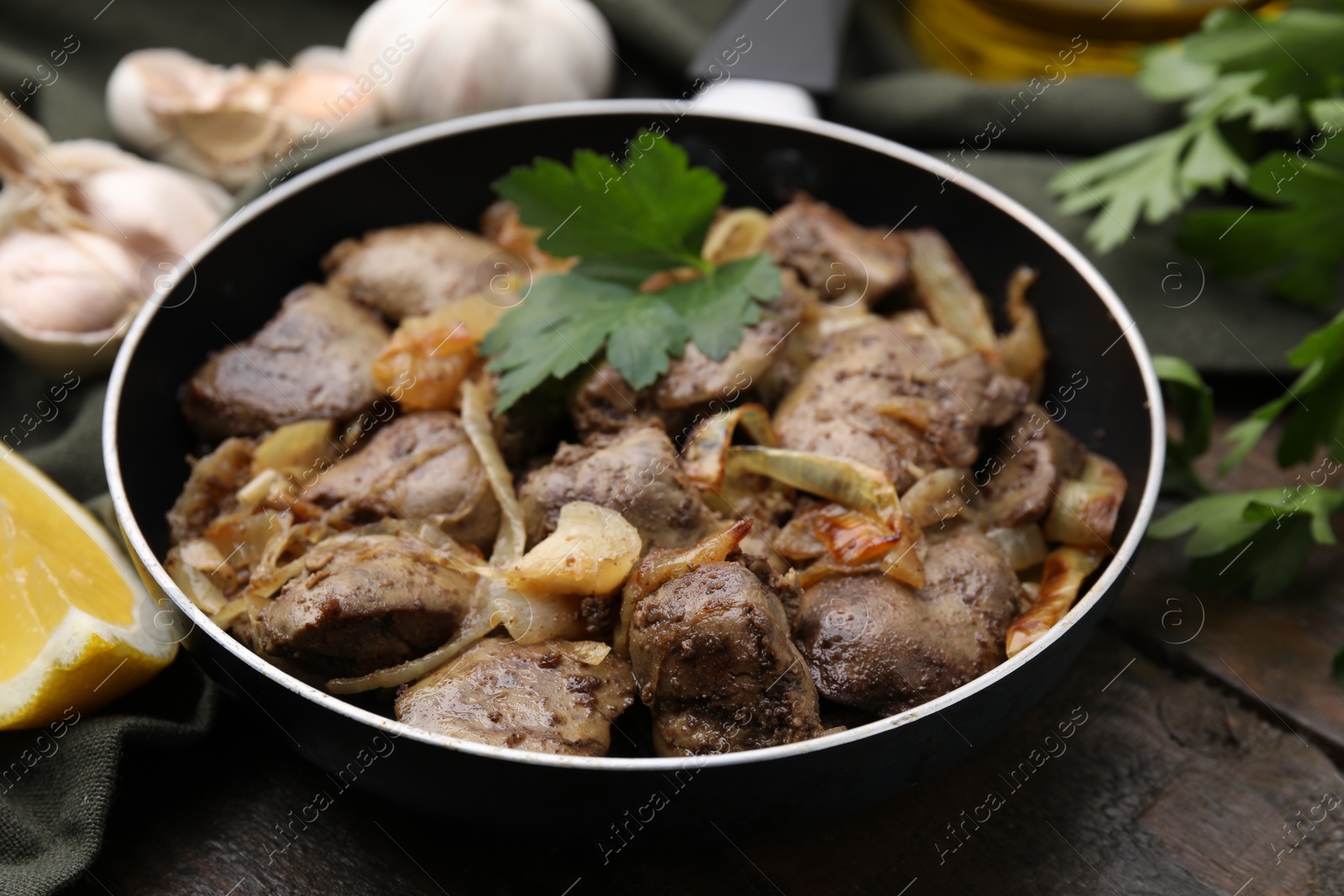 Photo of Tasty fried chicken liver with parsley and onion on wooden table, closeup