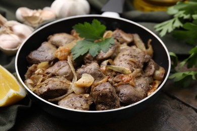 Tasty fried chicken liver with parsley and onion on wooden table, closeup