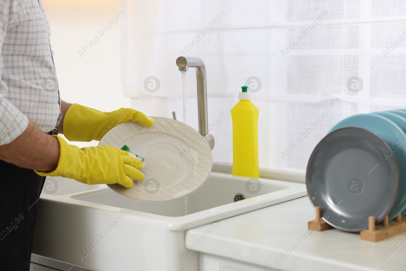 Photo of Man in protective gloves washing plate above sink in kitchen, closeup