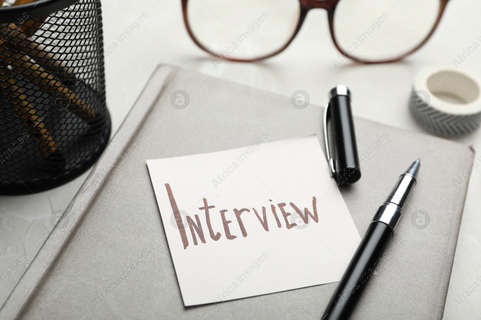 Photo of Reminder note about job interview and stationery on table, closeup