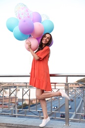 Photo of Cheerful young woman with color balloons on city street