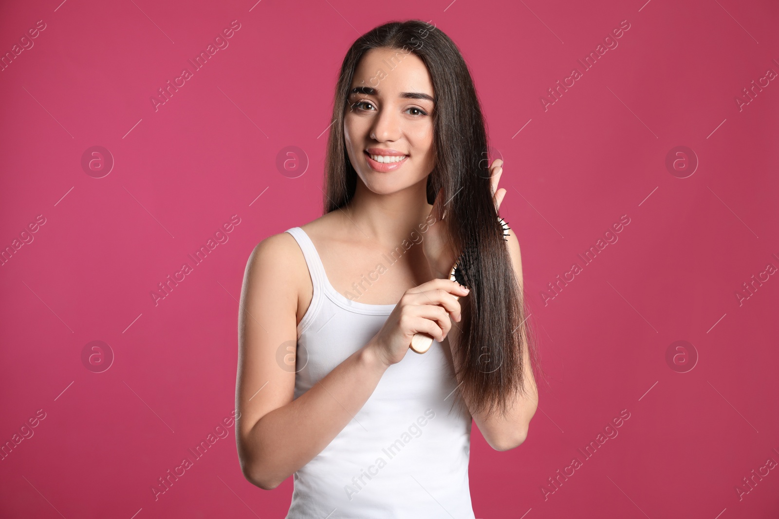 Photo of Beautiful smiling young woman with hair brush on color background