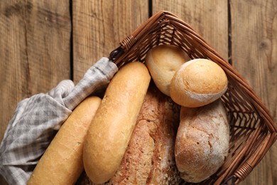 Photo of Wicker basket with different types of bread on wooden table, top view