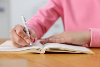 Young woman writing in notebook at wooden table, closeup