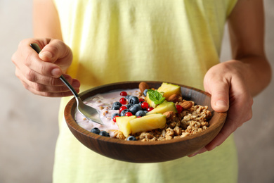 Woman eating tasty granola with yogurt, sliced pineapple and berries for breakfast, closeup