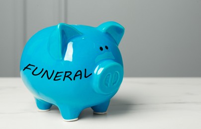 Image of Money for funeral expenses. Light blue piggy bank on white marble table